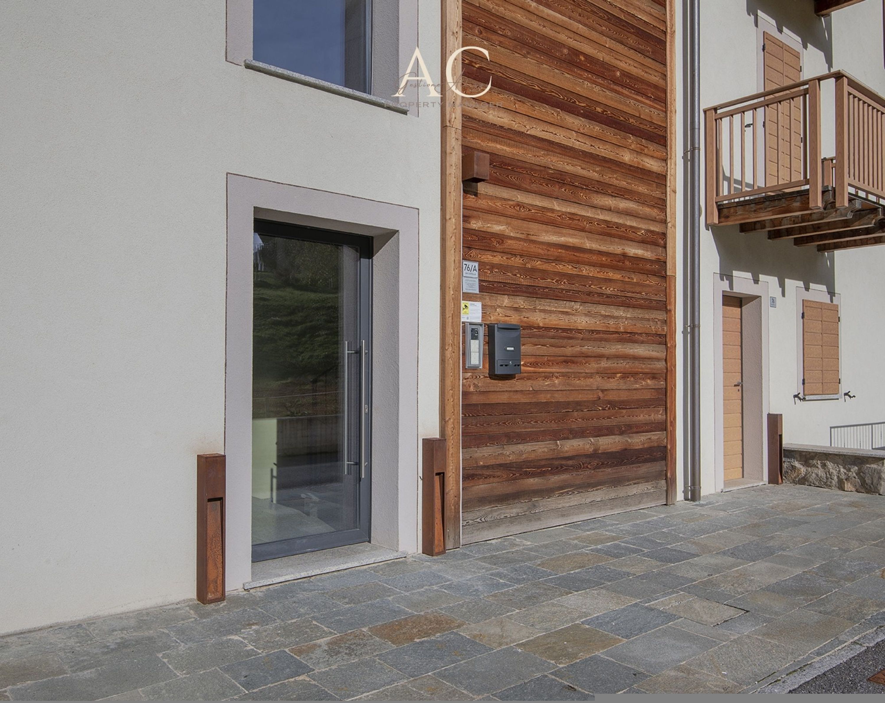 A modern building with a wooden panel facade, a glass door entrance, and a stone-paved ground.
