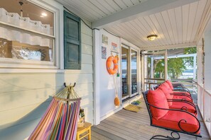 Eine überdachte Veranda mit Holzboden, eine Reihe roter gepolsterter Stühle, ein gestreiftes Stoffstück und ein Rettungsring an der Wand.
