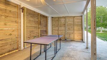 A covered outdoor area with a ping pong table, wooden walls, and a ceiling fan.