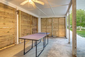 Ein überdachter Außenbereich mit Tischtennisplatte, Holzwänden und Deckenventilator.