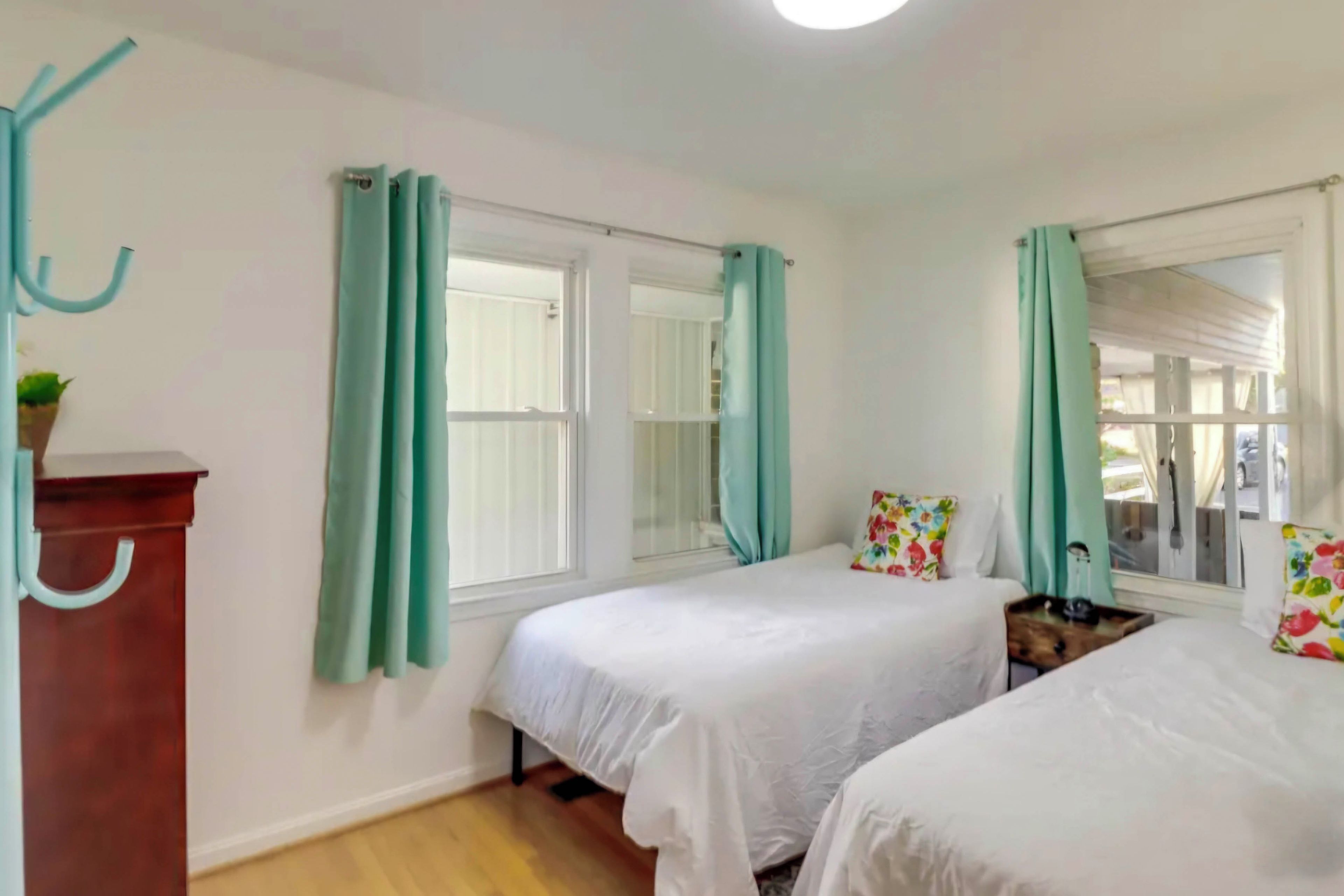 A bedroom with two beds, teal curtains, a wooden dresser, and a window with a view.