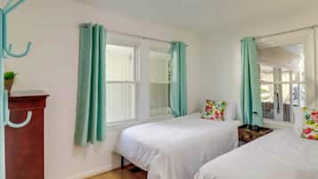 A bedroom with two beds, teal curtains, a wooden dresser, and a window with a view.