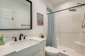 A bathroom with a white bathtub, a toilet, a sink with a faucet, a shower with a curtain, and a mirror on the wall. - Potomac River Getaway: Walk to Marina! (King George)