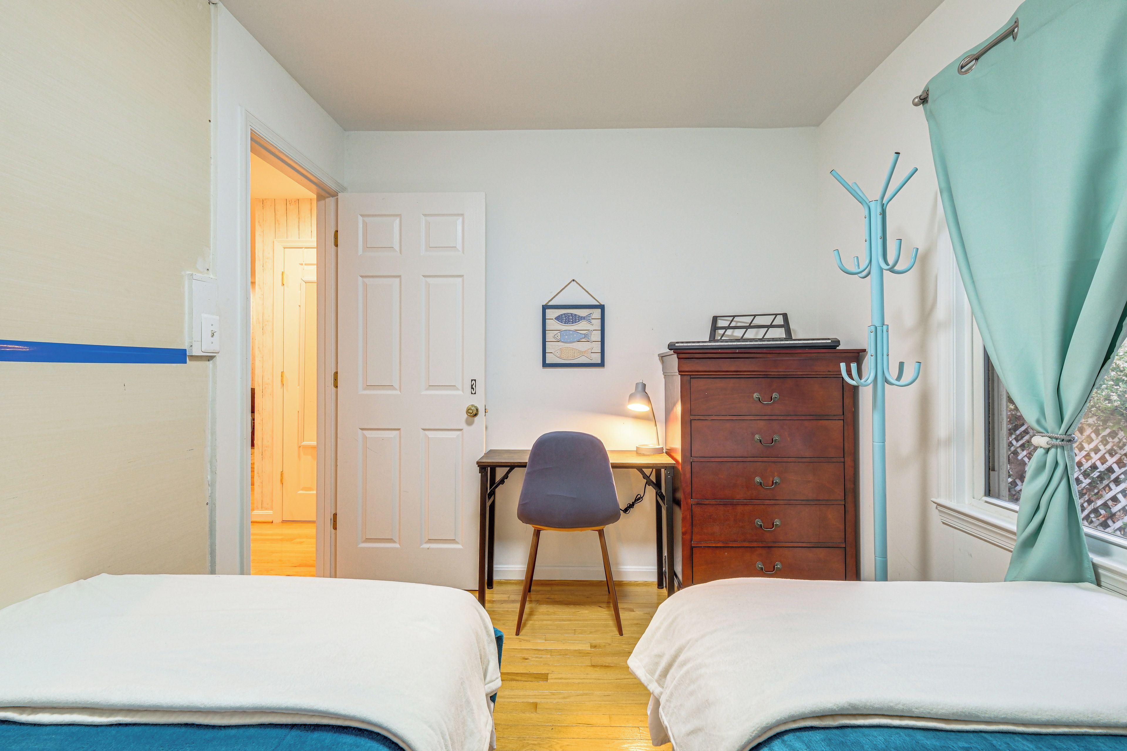 A room with two beds, a desk with a chair, a dresser, and a coat rack.