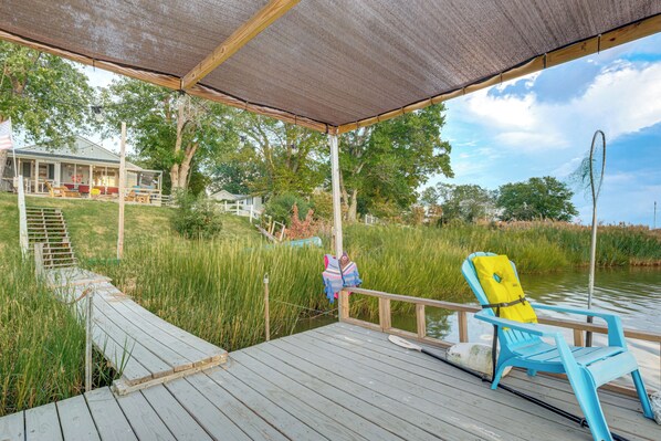 A wooden deck with a covered area, a chair, and a view of a house and natural surroundings. - Potomac River Getaway: Walk to Marina! (King George)