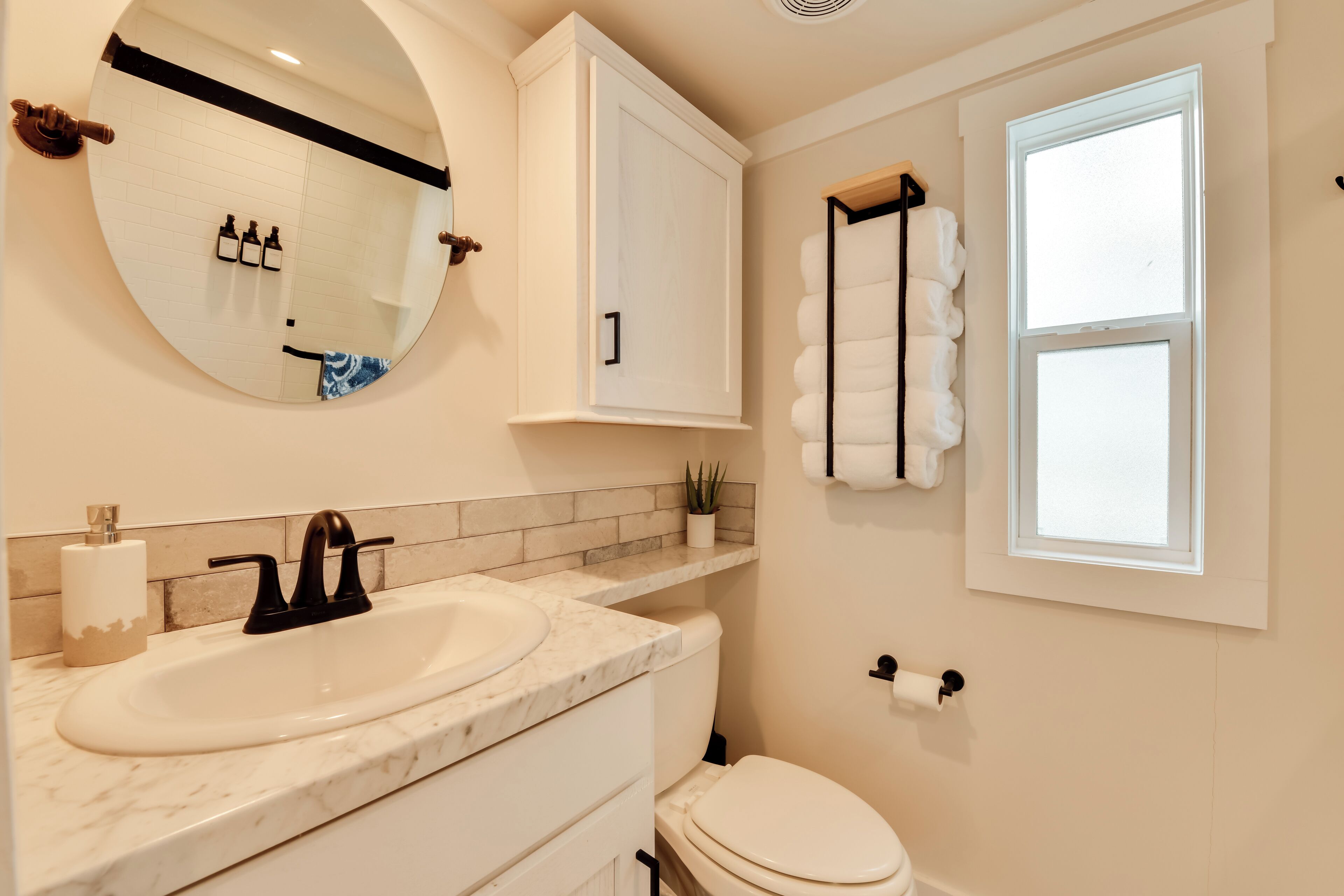 A bathroom with a white sink, a mirror, a toilet, and a window.