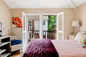 A bedroom with a bed, a chair, a desk, a lamp, and a large window with shutters. - Stylish Museum Apt 3 Comfort & Culture Combined 1 Bedroom Duplex (Houston)