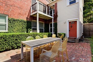 A patio with a table and chairs, a red door, and a brick wall. - Stylish Museum Apt 3 Comfort & Culture Combined 1 Bedroom Duplex (Houston)