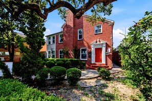 A red brick building with a white door and windows, surrounded by greenery and a clear sky. - Stylish Museum Apt 3 Comfort & Culture Combined 1 Bedroom Duplex (Houston)