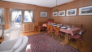 Comedor con una mesa de madera dispuesta para cuatro personas, rodeada de sillas con cojines rosados.