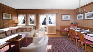 Una habitación luminosa con un sofá, sillas, una mesa de comedor para cuatro personas y un ventanal con cortinas.