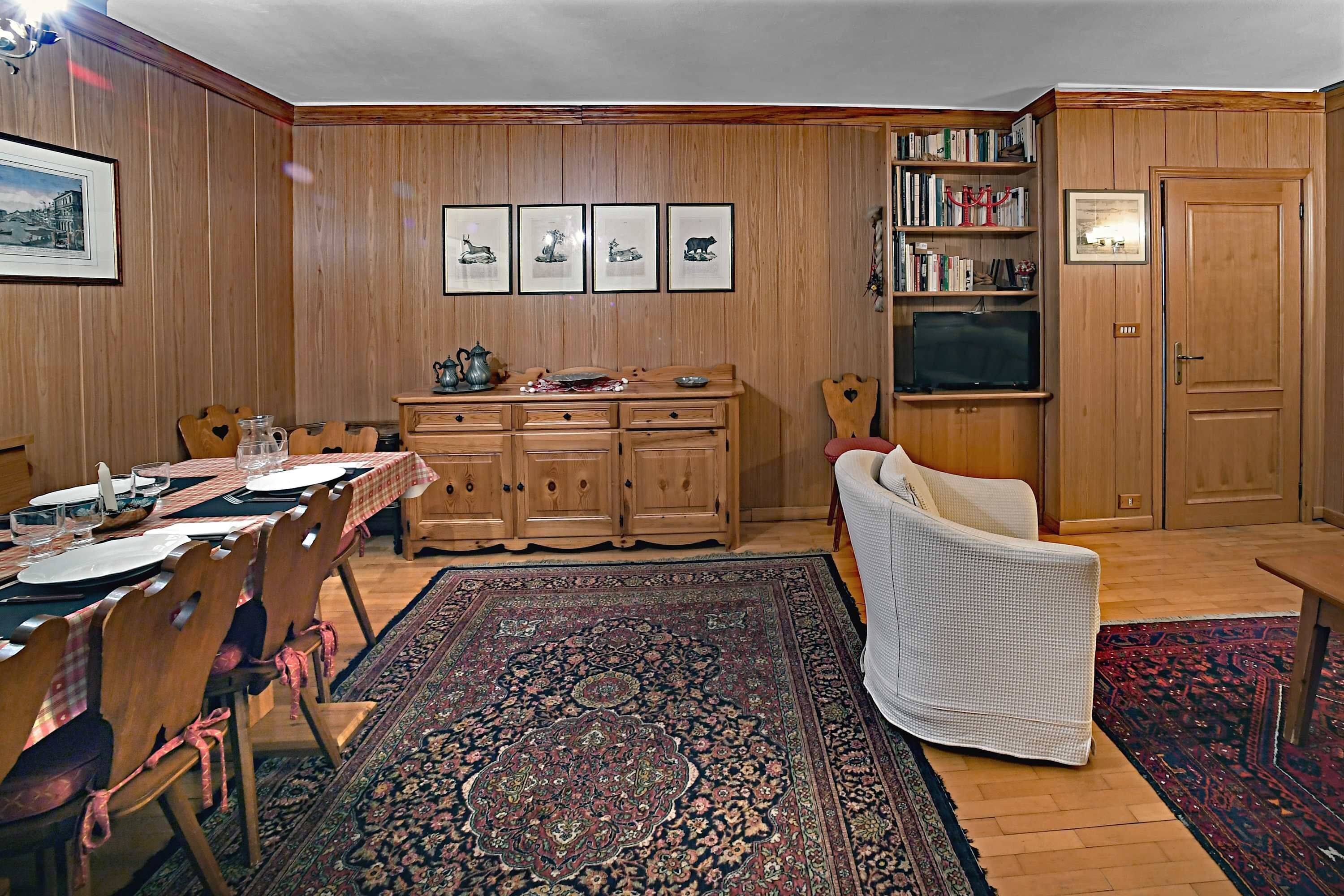 Un comedor con una mesa de madera dispuesta para cuatro personas, un mueble de madera a juego y un sillón blanco.