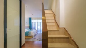 Ein modernes Hotelzimmer mit einem großen Bett, einer Holztreppe und einer Glastür zu einem anderen Raum.