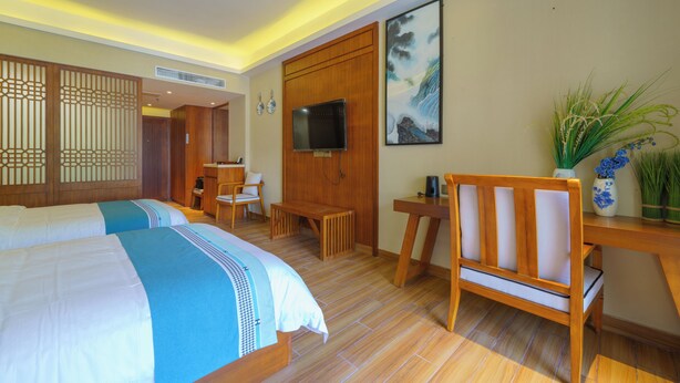 Ein Hotelzimmer mit zwei Betten, einem Schreibtisch, einem Sessel, einem Fernseher und einem Bild an der Wand.