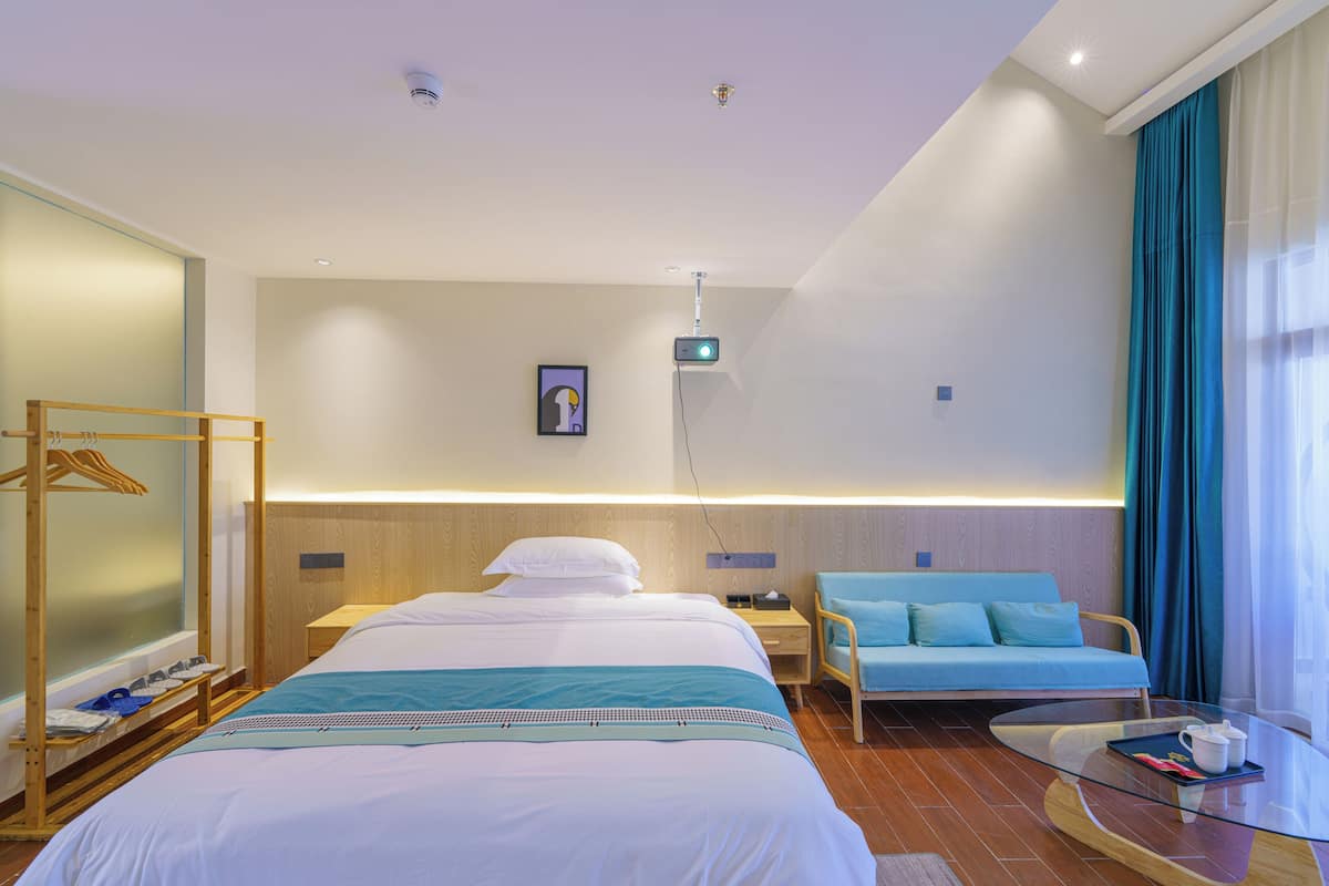 A hotel room with a bed, a seating area with a sofa, a small table, and a hanging light fixture.