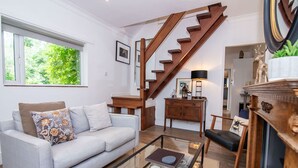 A living room with a light grey sofa, a glass coffee table, a wooden staircase, and a fireplace with a mirror and decorative items. - Host Stay Terrace on Canal (Worcester)