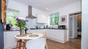 A modern kitchen with white cabinets, a round dining table with chairs, and a vase of flowers. - Host Stay Terrace on Canal (Worcester)