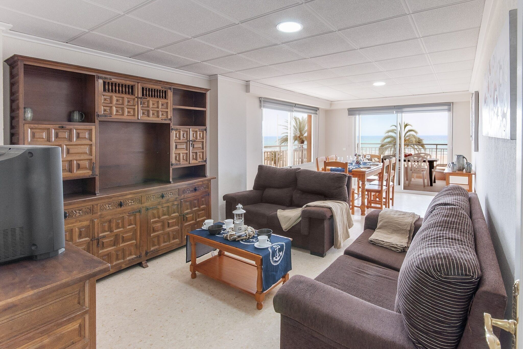 Ein Wohnzimmer mit einer Couch, einem Couchtisch und einem Fernseher. Es gibt einen Holzschrank mit mehreren Fächern.
