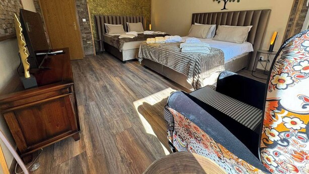 Une chambre moderne avec deux lits, une commode en bois, un fauteuil à motifs et une décoration murale représentant un arbre.
