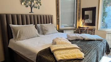 A neatly made bed with pillows and a blanket, a wall-mounted air conditioner, a window with a view, and a small table with a chair.