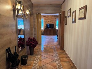 Ein Flur mit Holzwänden, Fliesenboden, einem Fernseher im Hintergrund und einem dekorativen Teppich.