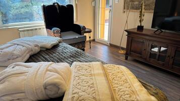 A bedroom with two beds, a large window, a television, and a stone wall.