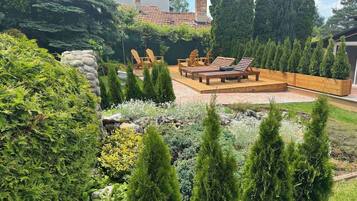 A landscaped backyard with a wooden deck, lounge chairs, and a variety of shrubs and trees.