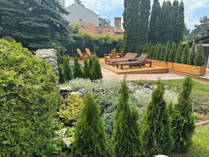 Un jardin aménagé à l’arrière de la maison, avec une terrasse en bois, des chaises longues et une variété d’arbustes et d’arbres.