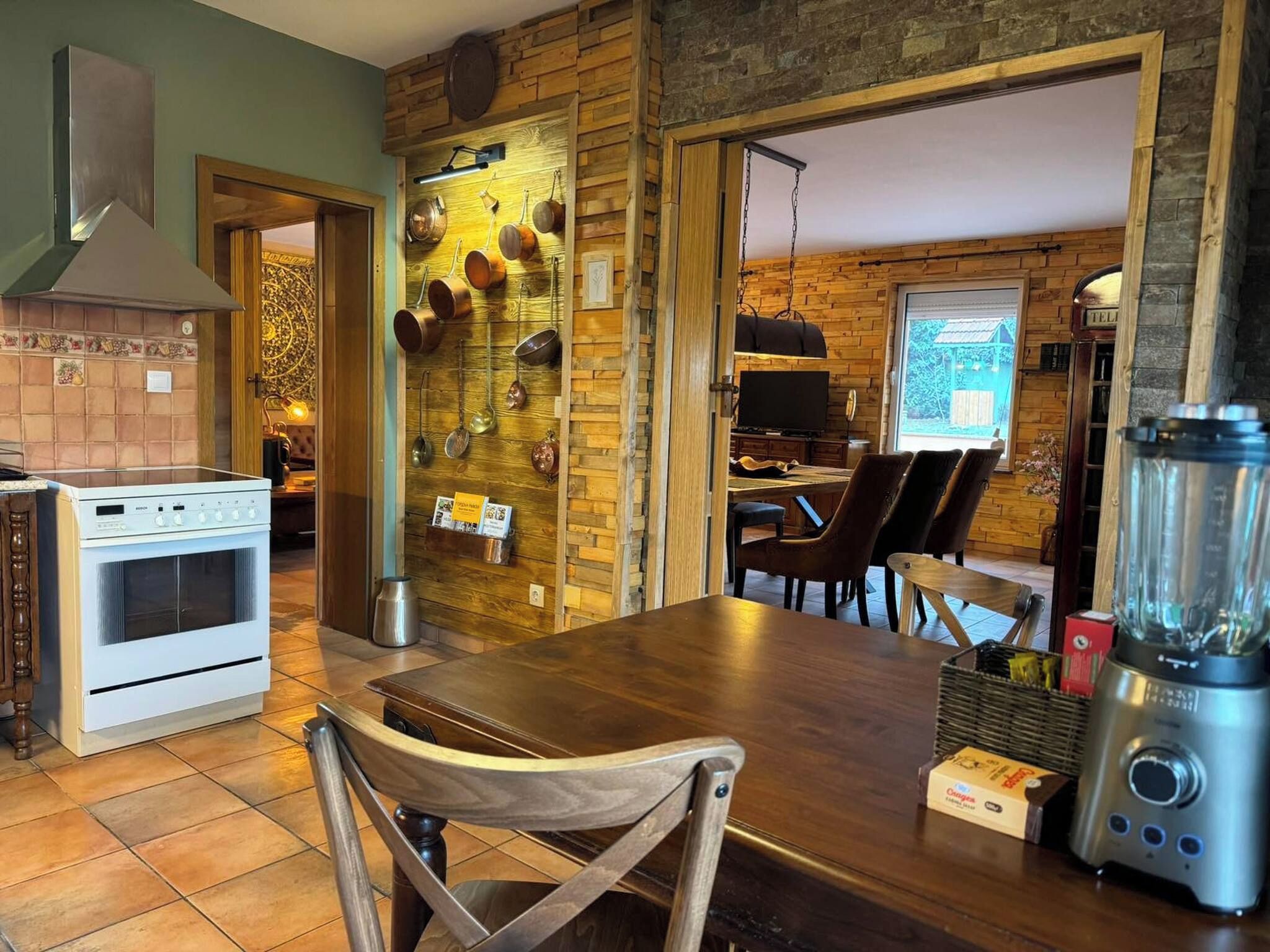 A kitchen with a stove, a dining table with chairs, a blender, and a wall-mounted pot rack.