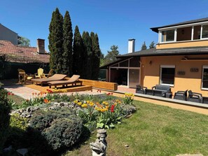 Ein Wohnhaus mit Terrasse, Sitzgelegenheit im Freien und einem Garten mit Blumen und Sträuchern.