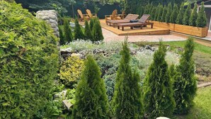Un jardin aménagé à l’arrière de la maison, avec une terrasse en bois, des chaises longues et une variété d’arbustes et d’arbres.