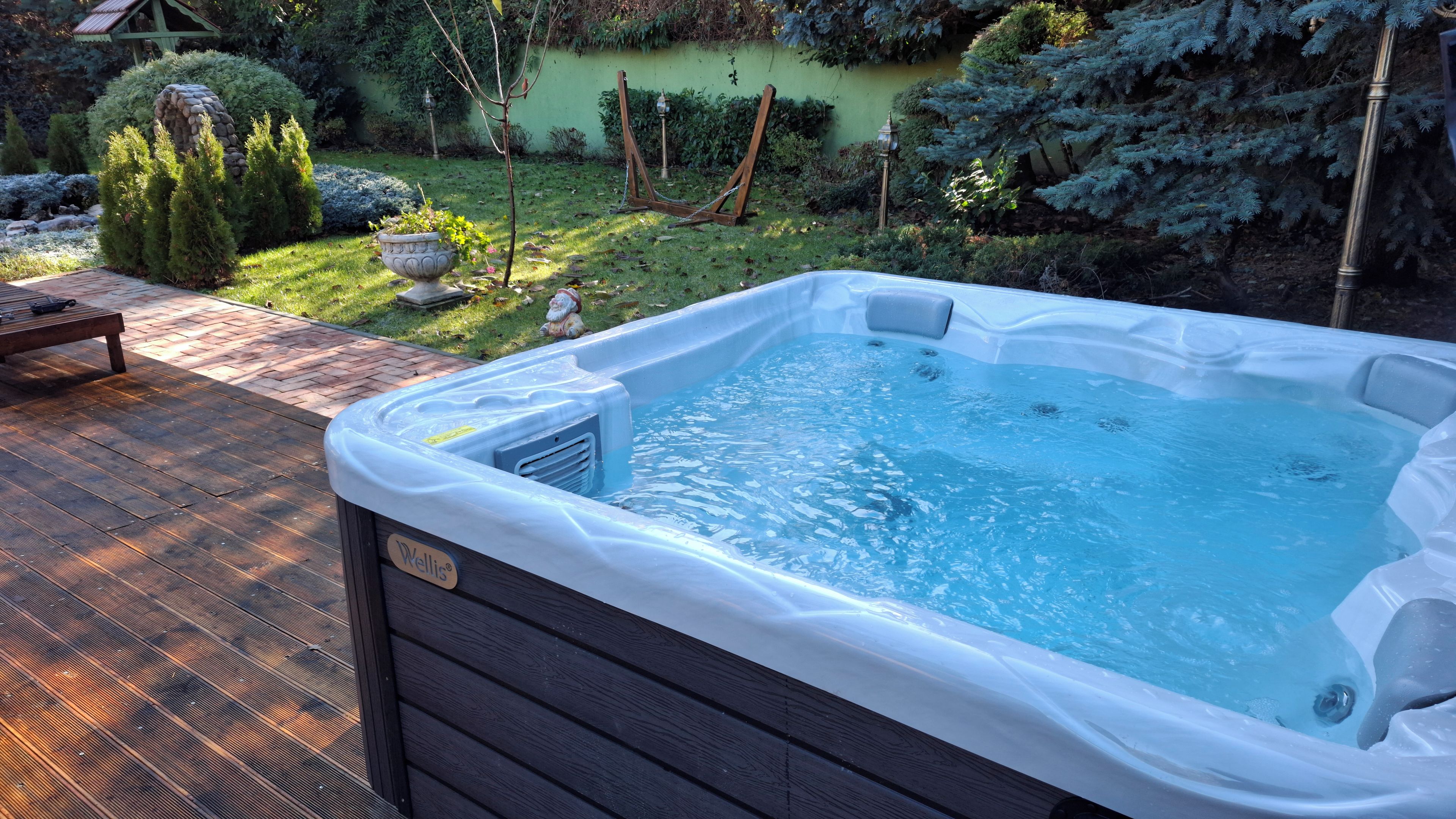 A hot tub with a wooden deck and a stone feature in the background.