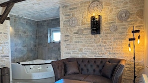 Ein gemütliches Zimmer mit Steinwand, Ledersofa, Holztisch und Whirlwanne.