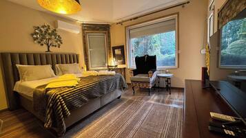 A modern bedroom with a large bed, a small table, a chair, and a TV.