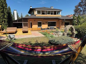 Une maison à deux étages dotée d’un patio, d’un espace salon extérieur et d’un hamac.