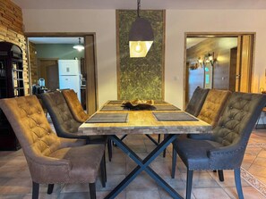 Un coin repas comprenant une table en bois, quatre chaises rembourrées et un luminaire suspendu.