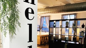 A modern interior with a large 'hello' sign, a wooden floor, a black bookshelf, and a hanging plant. - Chic 2-bedroom Urban Loft Condo Near Rogers Place Ice District Downtown Edmonton (Edmonton)