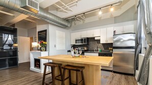 A modern kitchen with a central island, stainless steel appliances, and wooden bar stools. - Chic 2-bedroom Urban Loft Condo Near Rogers Place Ice District Downtown Edmonton (Edmonton)