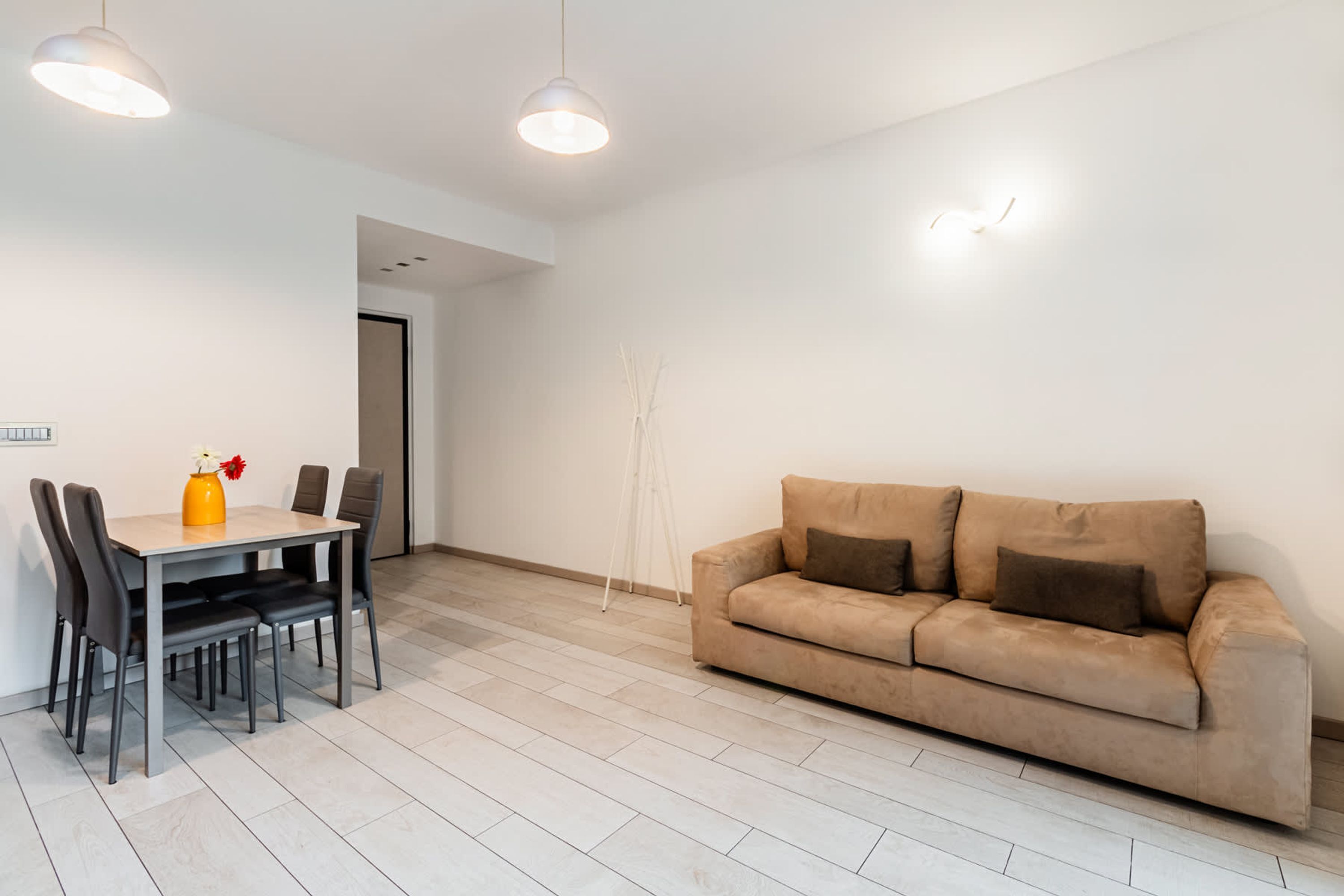 A modern living room with a beige sofa, a dining table with chairs, and pendant lighting.