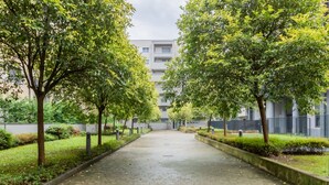 Un chemin pavé bordé d’arbres, avec un bâtiment en arrière-plan.