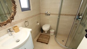Un baño con lavamanos blanco, una caja de madera, un inodoro y una cabina de ducha de vidrio.