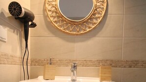 A bathroom with a round mirror, white sink, and wooden cabinets. - Schinos by Frangki (Aegina)