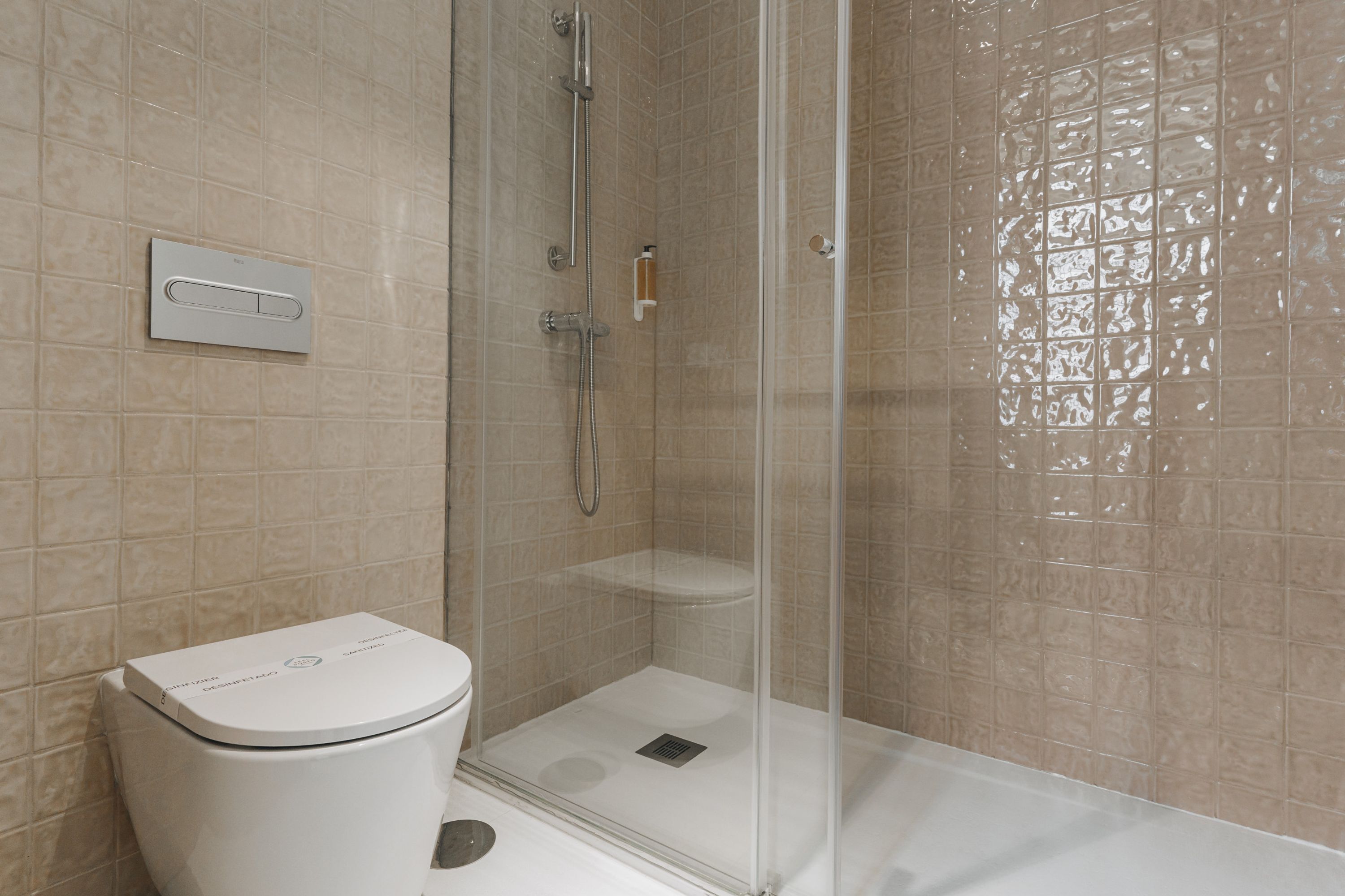 Un baño con inodoro, ducha con puerta de vidrio y pared de azulejos.