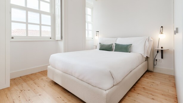 A bedroom with a large bed, two bedside tables with lamps, a window, and wooden flooring. - Feel Porto Cl Rigos Charm Flat 3 1 (Porto)