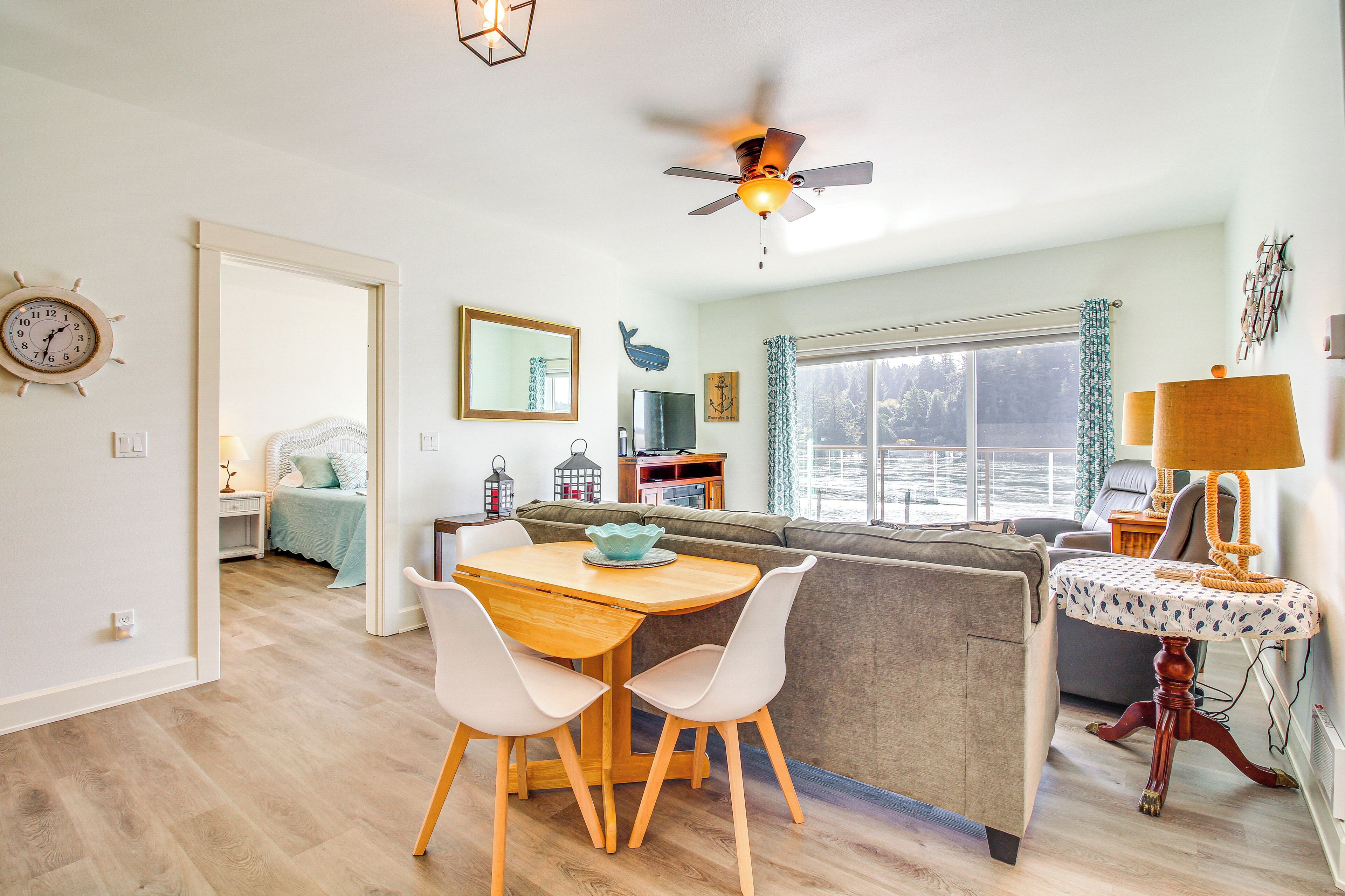 A well-lit living room with a wooden dining table, white chairs, a sofa, and a ceiling fan.