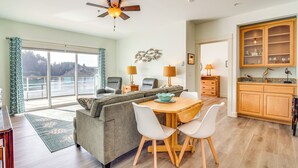 A modern living room with a sofa, dining table, and chairs. There is a ceiling fan, a kitchen area with cabinets, and a view of the outdoors through large windows. - Riverfront Apt in Old Town Florence! (Florence)