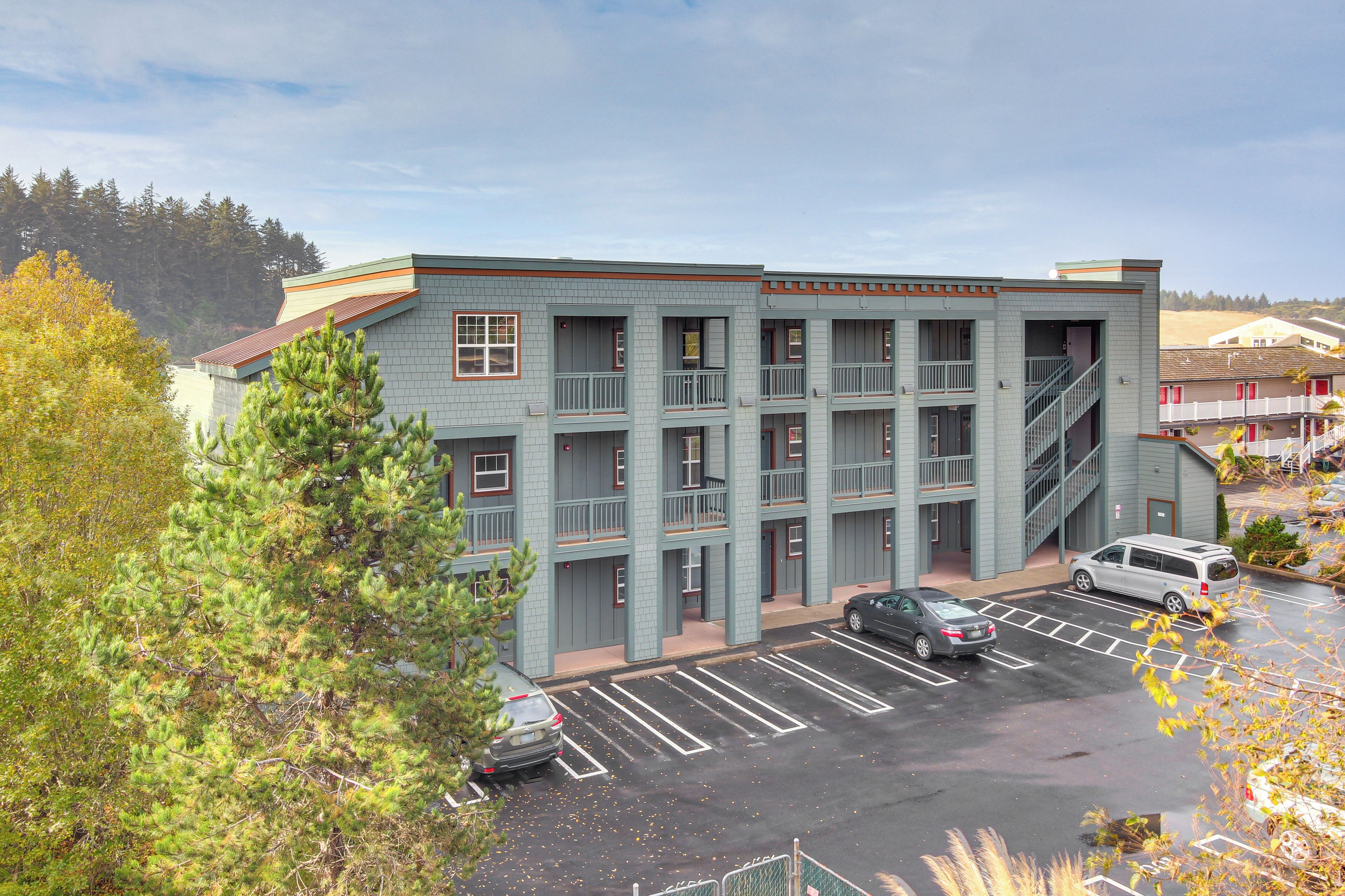 A multi-story building with a parking lot, a staircase, and a view of trees.