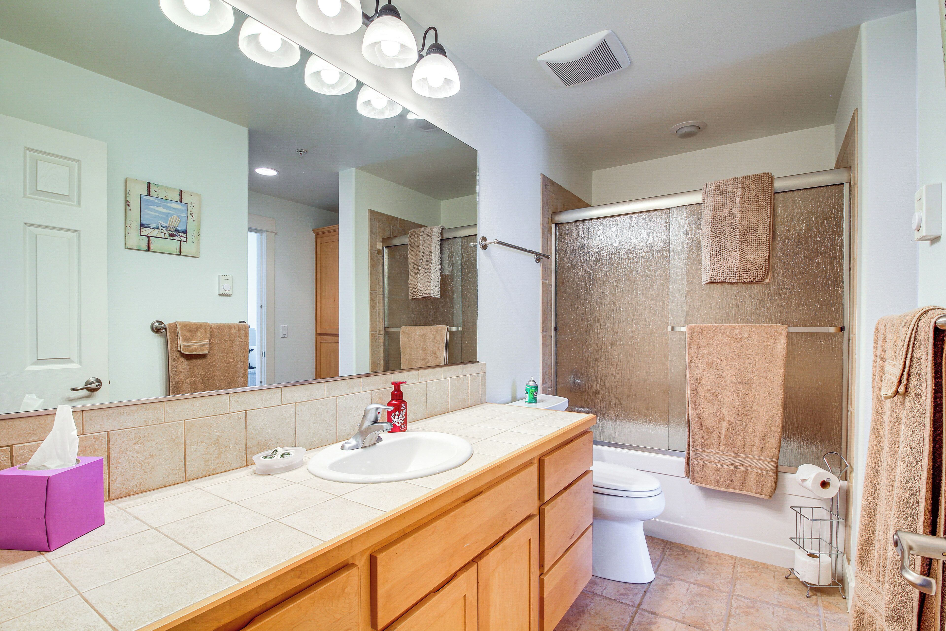 A bathroom with a large mirror, a sink, a toilet, and a shower.