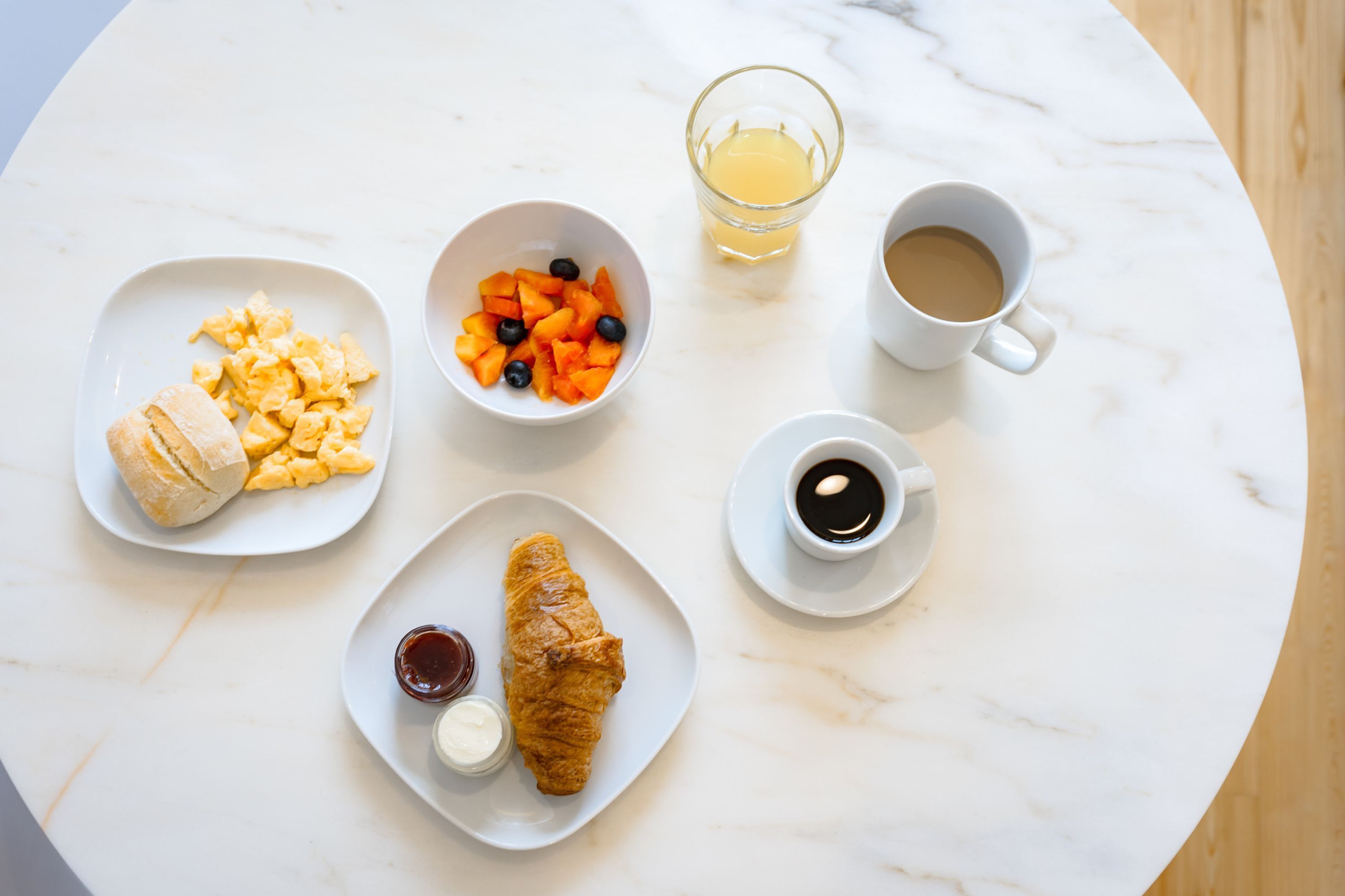 A breakfast setting with scrambled eggs, croissants, fruit, and coffee on a marble table.