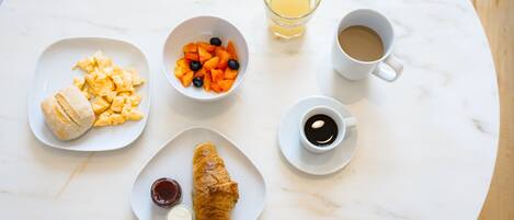 A breakfast setting with scrambled eggs, croissants, fruit, and coffee on a marble table.